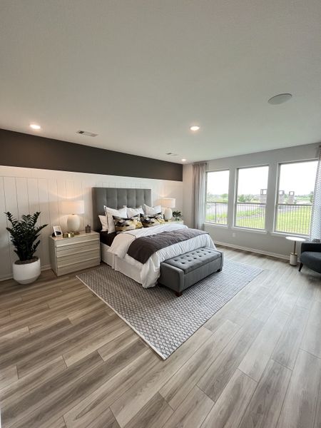 A spacious bedroom with wooden floors, large windows, gray accents, and elegant decor.