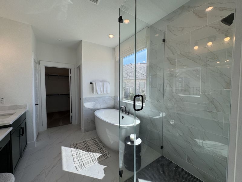 A bright bathroom featuring a freestanding tub, glass shower, and marble tiles with contemporary fixtures.