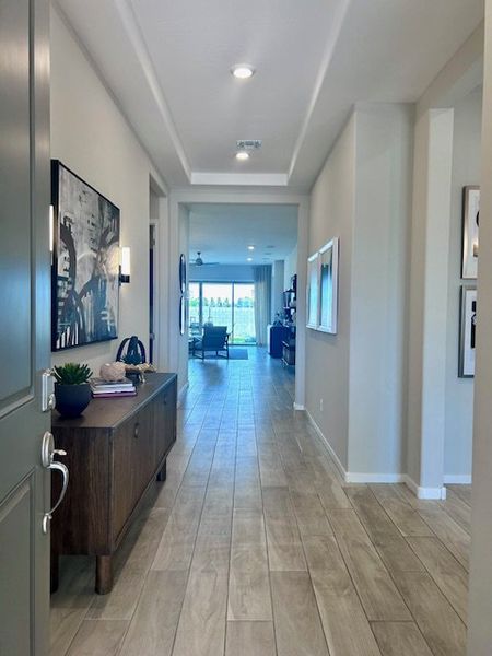 A bright, welcoming hallway with wood-style flooring, modern art, and an inviting view to the living area. A bright, welcoming hallway with wood-style flooring, modern art, and an inviting view to the living area.