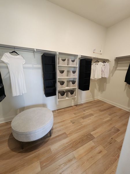 A spacious walk-in closet with wooden flooring, organized shelving, and a cozy ottoman for seating. A spacious walk-in closet with wooden flooring, organized shelving, and a cozy ottoman for seating.