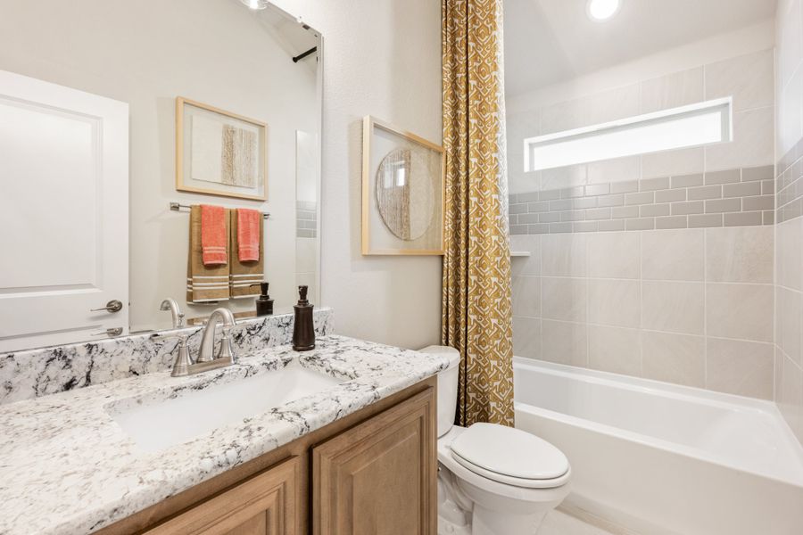 Full bathroom with granite countertop vanity, tiled tub-shower combo, and gold patterned curtain