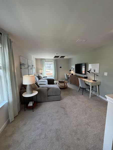 A cozy living space with a plush sectional, a desk, and large windows, creating a bright and inviting atmosphere.