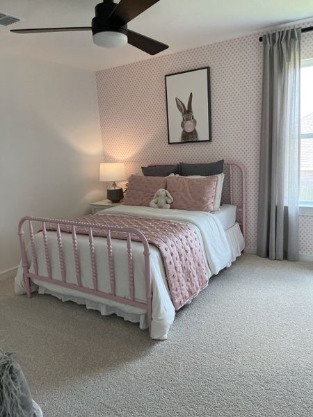 Cozy bedroom with a pink metal bed, patterned wallpaper, and plush bedding, accented by a whimsical bunny print.