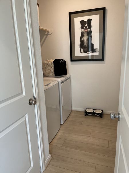 A cozy laundry room featuring modern appliances, light wood flooring, and a charming dog portrait for a stylish touch. A cozy laundry room featuring modern appliances, light wood flooring, and a charming dog portrait for a stylish touch.