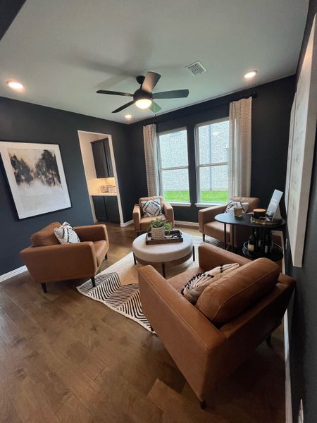 A cozy living room with dark walls, warm leather chairs, a round coffee table, and chic modern decor.