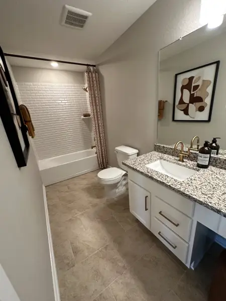 A chic bathroom with granite countertops, tiled floors, and modern fixtures, complemented by elegant wall art.