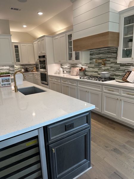 A modern kitchen featuring sleek white cabinetry, a large island with a gold faucet, and a stylish tiled backsplash.