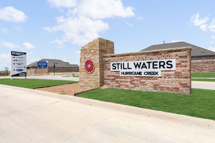 Brick entrance monument sign for Still Waters Hurricane Creek neighborhood with green landscaping and homes in background