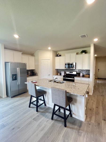 A modern kitchen with granite countertops, white cabinets, stainless steel appliances, and sleek wood flooring.