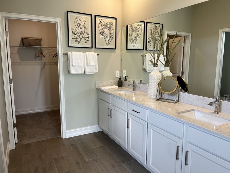 A contemporary bathroom featuring a double vanity, neutral decor, and an adjacent walk-in closet with ample space.