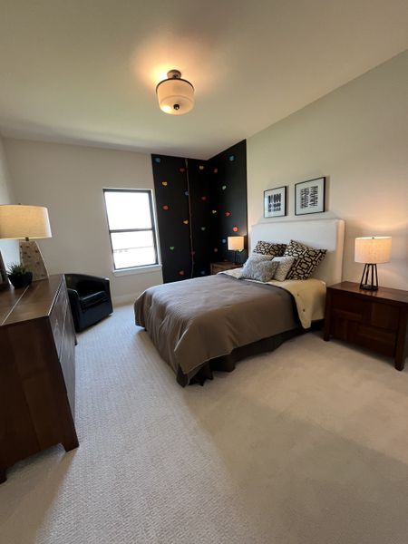 Cozy bedroom with a climbing wall accent, neutral tones, stylish lighting, and wooden furniture.