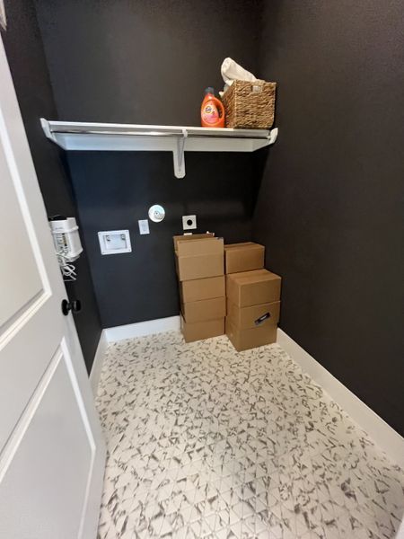 A practical laundry room with geometric tile flooring, deep gray walls, and white shelving for storage essentials.