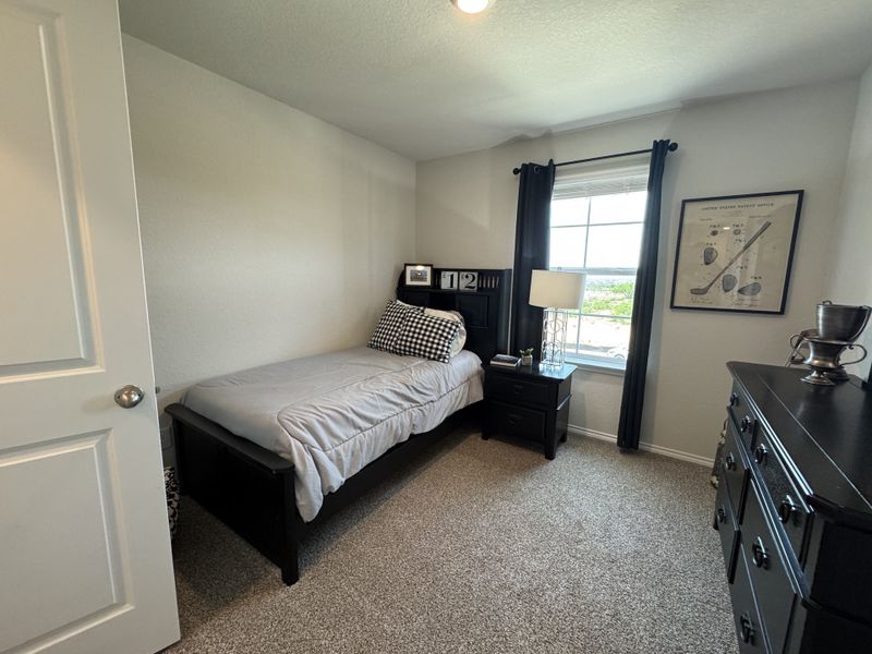 A cozy bedroom with a single bed, black furniture, and soft carpeting, featuring a large window and tasteful decor.