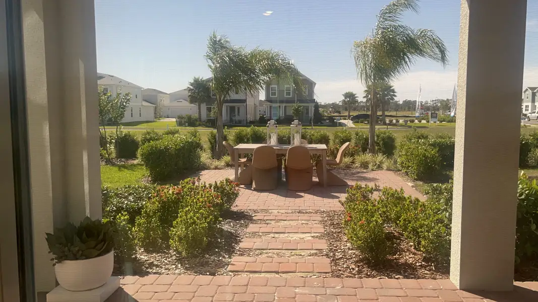 A charming patio with palm trees, a dining set, and lush landscaping.