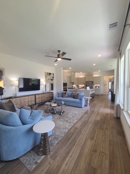 An elegant living area with blue sofas, wood flooring, and a seamless open layout connecting to a modern kitchen.