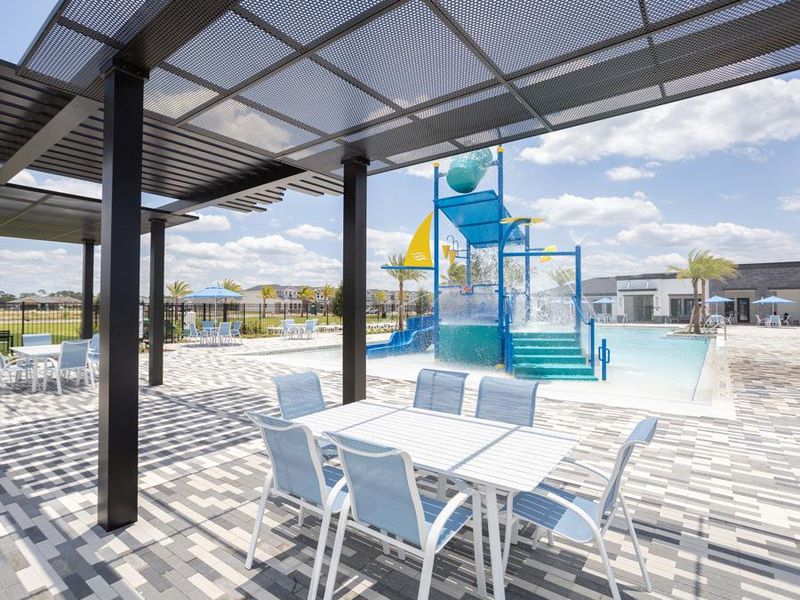 The pool area features lounge chairs, open and covered seating, and a splash pad with a water slide.