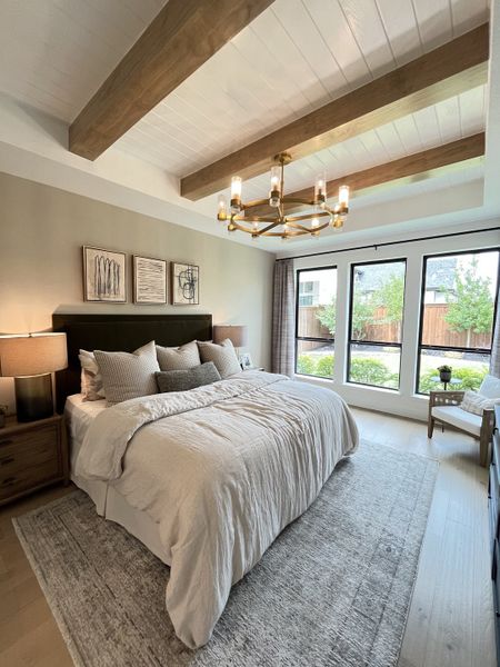 A cozy bedroom featuring exposed wooden beams, a plush bed with soft linens, and large windows offering a serene garden view.