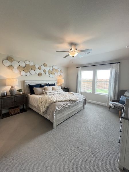 A cozy bedroom with neutral tones, soft carpeting, layered bedding, textured wall decor, and ample natural light. A cozy bedroom with neutral tones, soft carpeting, layered bedding, textured wall decor, and ample natural light.