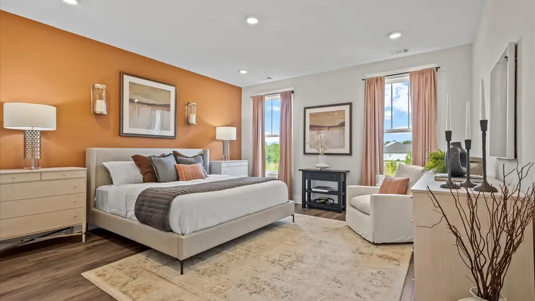 Inviting primary suite with floor to ceiling windows, hardwood flooring, and accent wall at Iris Meadows by DRB Homes