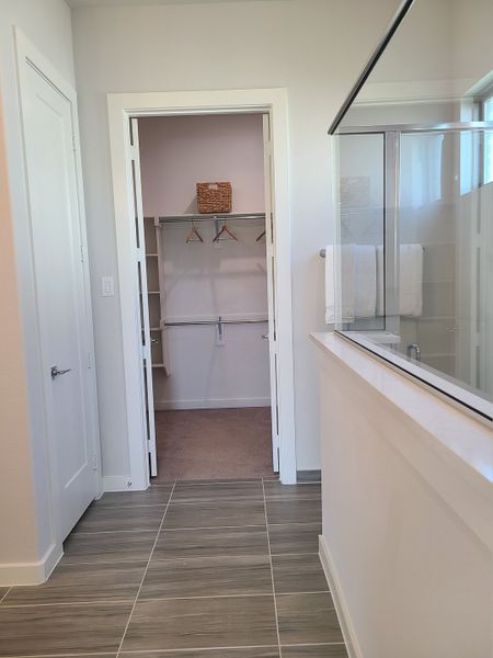 A sleek bathroom with gray tile flooring leads to a spacious walk-in closet, featuring modern shelving and a glass shower.