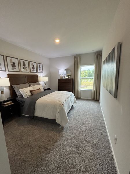 A cozy bedroom featuring plush carpeting, elegant art, and soft lighting with a view of the serene outdoors.
