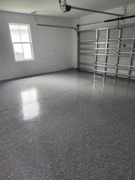 A spacious garage featuring a speckled epoxy floor, a large window, and a modern overhead door. Perfect for versatile utility and storage. A spacious garage featuring a speckled epoxy floor, a large window, and a modern overhead door. Perfect for versatile utility and storage.