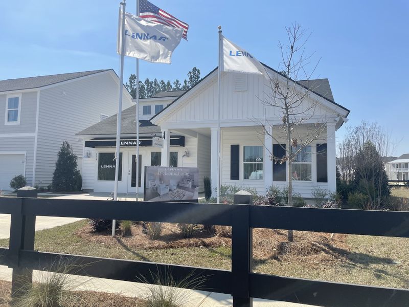 A charming white home with flags and a manicured lawn in Sweetgrass at Summers Corner: Arbor Collection by Lennar (Ridgeville, SC).