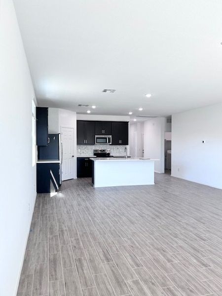 A spacious kitchen with dark cabinets, sleek appliances, an island, and wood-look flooring. Bright and modern space.