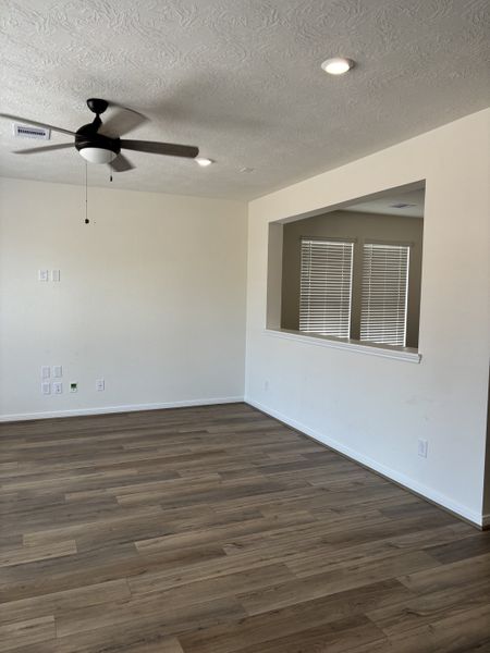 A modern living space with sleek laminate flooring, neutral walls, and a ceiling fan, featuring a cut-out window for added light.