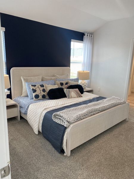 A luxurious master bedroom with a bold navy accent wall, elegant furnishings, and plush carpeting.