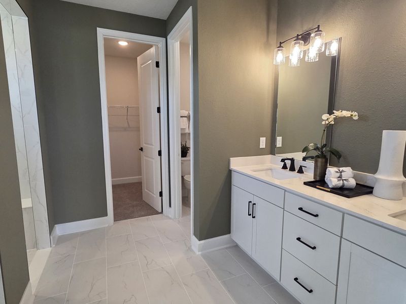 A modern bathroom featuring a sleek white vanity, elegant light fixtures, and a spacious walk-in area with marble accents.