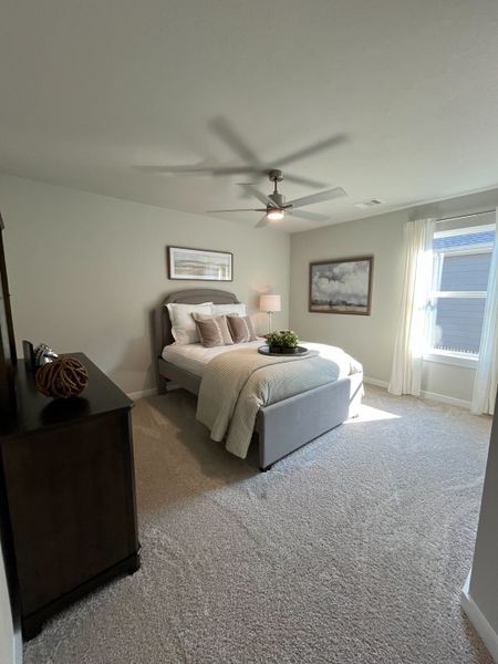 A cozy bedroom featuring a plush bed, soft carpeting, modern ceiling fan, and large window with soft natural light. A cozy bedroom featuring a plush bed, soft carpeting, modern ceiling fan, and large window with soft natural light.