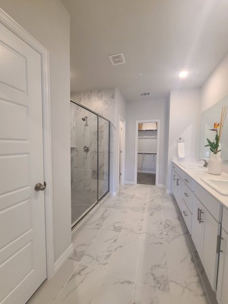 A spacious bathroom featuring marble-style tiles, a double vanity, and a glass-enclosed shower.