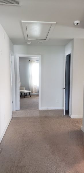 A well-lit hallway with neutral walls, plush carpeting, and access to a bright, inviting room. A well-lit hallway with neutral walls, plush carpeting, and access to a bright, inviting room.