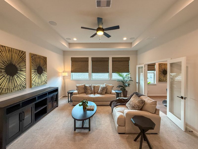 A cozy living room with plush seating, abstract wall art, and a ceiling fan, featuring natural light from large windows.
