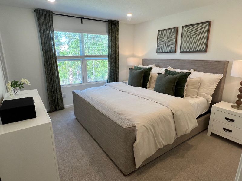 A cozy bedroom features a plush bed, elegant decor, large window with lush views, and tasteful artwork.