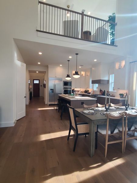 A modern open-plan kitchen with high ceilings, sleek island, and elegant dining area, featuring warm wood flooring.