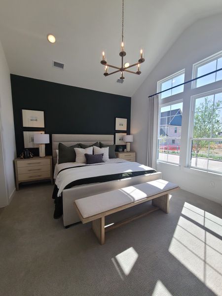 A modern bedroom with a vaulted ceiling, elegant chandelier, and large windows allowing natural light to pour in.