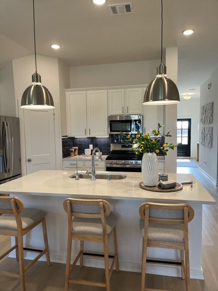A modern kitchen with sleek pendant lights, white cabinetry, and a stylish island complete with cozy bar stools. A modern kitchen with sleek pendant lights, white cabinetry, and a stylish island complete with cozy bar stools.