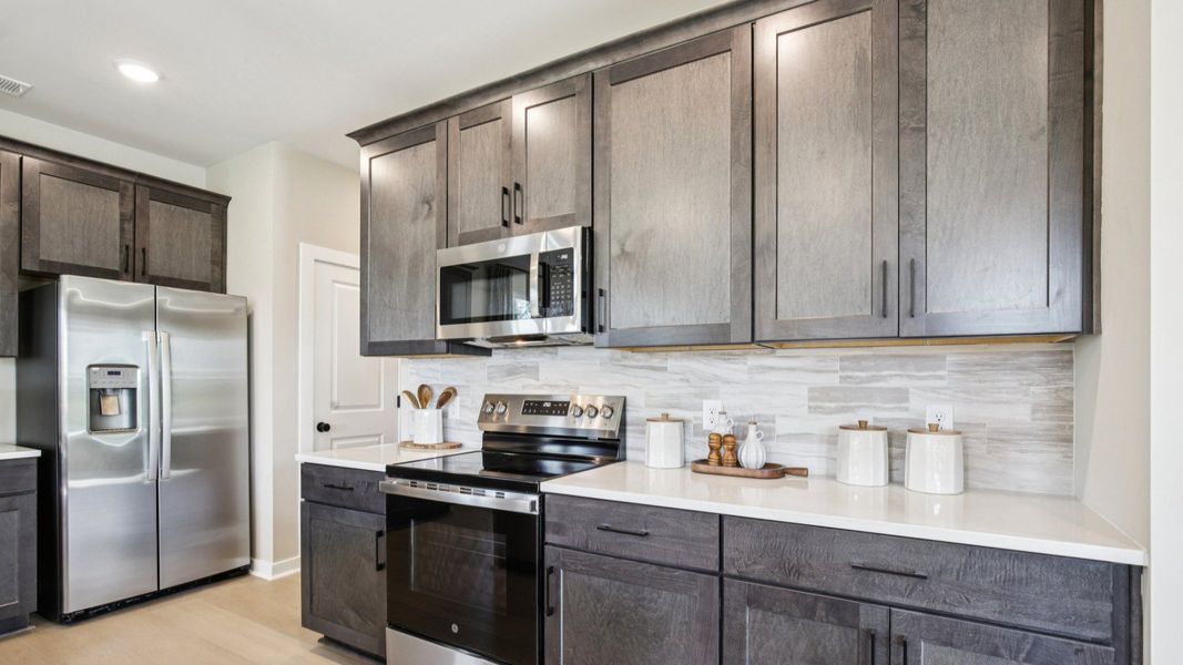 Upscale finishes including quartz countertops, stained cabinets, tile backsplash, and black hardware