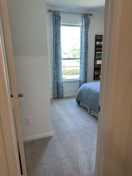 A cozy bedroom with soft carpet, blue bedding, and patterned curtains framing a bright window.