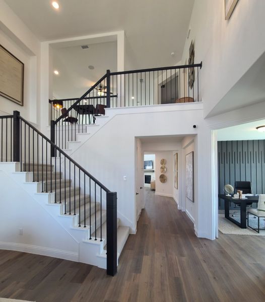 A modern interior featuring an elegant staircase, hardwood floors, and a bright, open hallway leading to a stylish office space.
