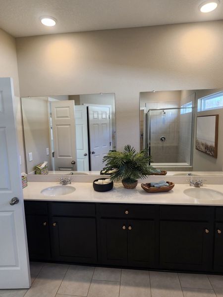 A spacious bathroom with dual sinks, dark cabinets, and elegant decor under soft recessed lighting.