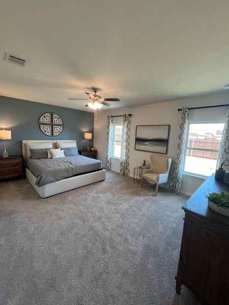 Spacious bedroom with a cozy bed, elegant decor, soft carpeting, and ample natural light through large windows.