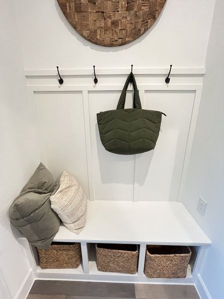 A cozy nook with a white bench, wicker baskets, wall hooks, and soft cushions for stylish storage and seating.