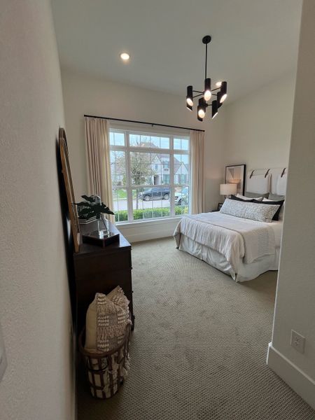 A cozy bedroom featuring a modern chandelier, large window, and neutral decor for a serene atmosphere.