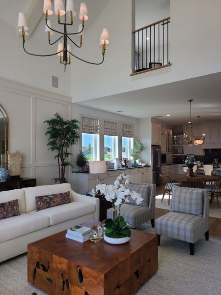 A spacious living room with elegant chandeliers, plush seating, a wooden coffee table, and open kitchen layout. A spacious living room with elegant chandeliers, plush seating, a wooden coffee table, and open kitchen layout.