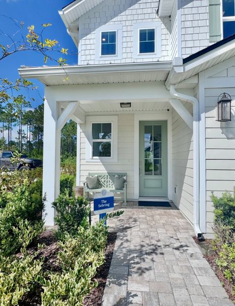 A charming white home with elegant trim and a cozy porch in Crosswinds at Nocatee by Riverside Homes (Ponte Vedra Beach, FL).