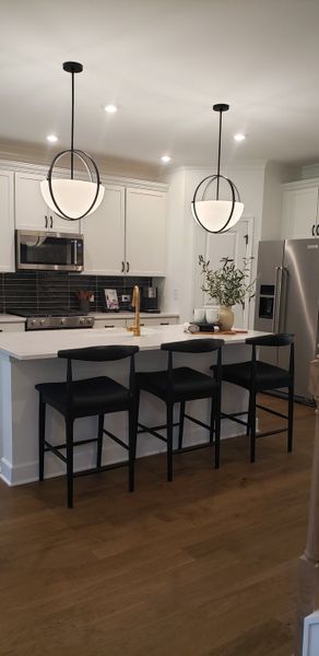 A modern kitchen with sleek black pendant lights, an inviting island, and stainless steel appliances.