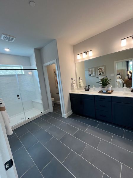 A modern bathroom featuring sleek gray tiles, a double vanity, and a glass shower enclosure with contemporary lighting.